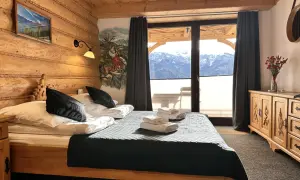 Przytulna sypialnia w stylu góralskim w Willi Kominiarski Wierch. Drewniane ściany, łóżko z czarną narzutą i widok na Tatry.