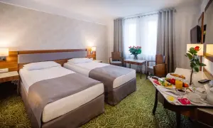 Pokój hotelowy z dwoma łóżkami, stolikiem z owocami i różami. Zastanawiasz się, ile kosztuje nocleg w hotelu?