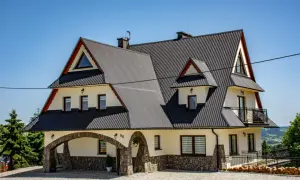 Willa pod Zielonym Wierchem w Zakopanem, z kamiennym łukiem i wielospadowym dachem, zaprasza na wypoczynek w górskim klimacie.