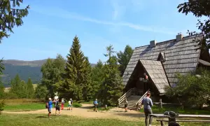 Bacówka PTTK pod Małą Rawką, drewniany schron turystyczny w otoczeniu zieleni, z kilkoma turystami na szlaku.