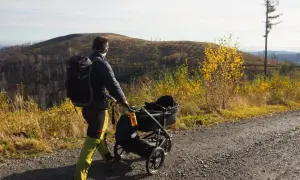 Wędrówka gdzie w góry z dzieckiem w wózku. Jesienny krajobraz, osoba z plecakiem pcha wózek po kamienistej drodze.