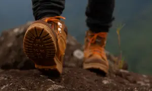 Brązowe buty trekkingowe z pomarańczowymi sznurówkami na kamienistym szlaku. Idealne buty w góry, zapewniające przyczepność i stabilność.