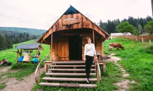 Kobieta przed bacówką u Jancoka, gdzie można kupić oscypki. W tle pasąca się krowa i górski krajobraz.