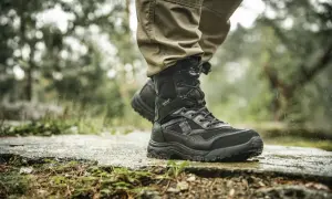 Czarne, wysokie buty trekkingowe na mokrej ścieżce. Idealne, jakie buty w góry jesienią, by stawiać pewne kroki w deszczu.