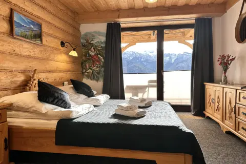 Przytulna sypialnia w stylu góralskim w Willi Kominiarski Wierch. Drewniane ściany, łóżko z czarną narzutą i widok na Tatry.