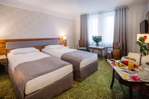 Pokój hotelowy z dwoma łóżkami, stolikiem z owocami i różami. Zastanawiasz się, ile kosztuje nocleg w hotelu?