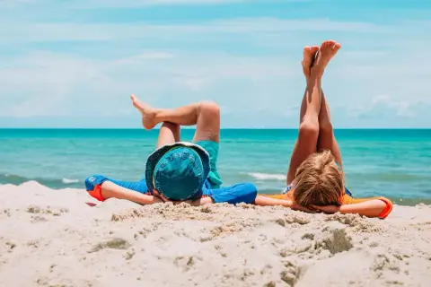 Dzieci leżą na plaży, marząc o wakacjach. Szukając noclegów nad morzem, warto pomyśleć o takich beztroskich chwilach.