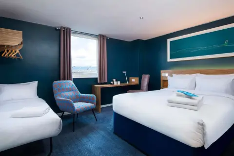 Pokój hotelowy z dwoma łóżkami, biurkiem i fotelem. Zastanawiasz się, ile kosztuje nocleg w Londynie?