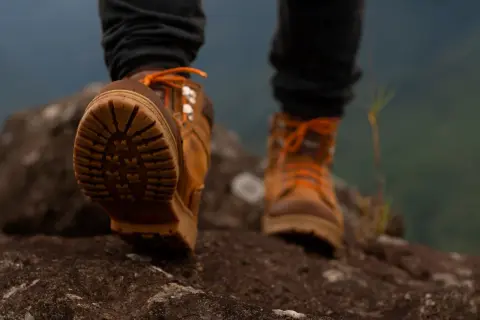 Brązowe buty trekkingowe z pomarańczowymi sznurówkami na kamienistym szlaku. Idealne buty w góry, zapewniające przyczepność i stabilność.