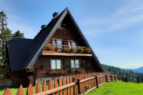 Drewniana bacówka na Maciejowej, otoczona zielenią i drewnianym płotem, z balkonem pełnym kwiatów.