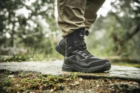 Czarne, wysokie buty trekkingowe na mokrej ścieżce. Idealne, jakie buty w góry jesienią, by stawiać pewne kroki w deszczu.