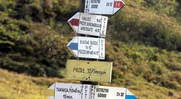 Znaki szlaku turystycznego PTTK. Wskazują kierunki i czas dojścia do różnych miejsc, np. Ustrzyki Górne, Tarnica. Czarny szlak oznacza trasę o średnim stopniu trudności.