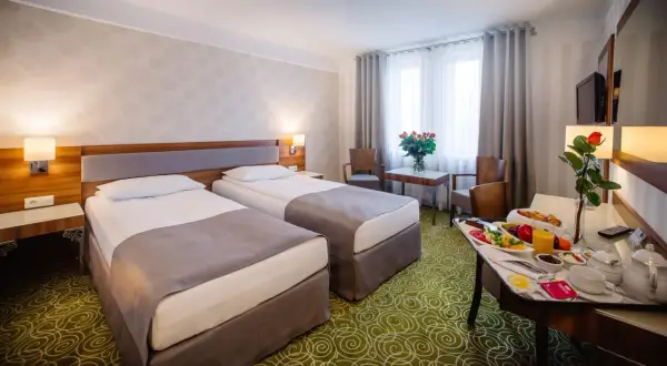 Pokój hotelowy z dwoma łóżkami, stolikiem z owocami i różami. Zastanawiasz się, ile kosztuje nocleg w hotelu?