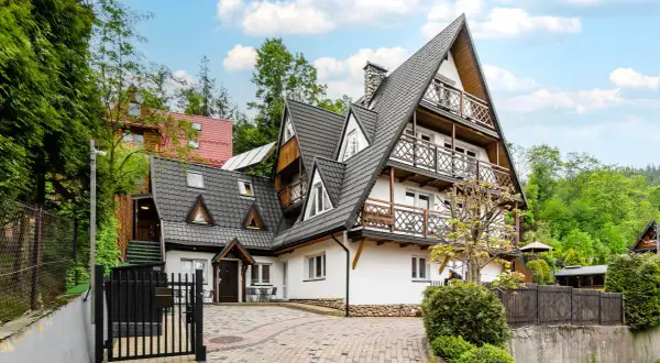 Urokliwa bacówka na Bundówkach, z drewnianymi balkonami i kamiennym cokołem, otoczona zielenią.