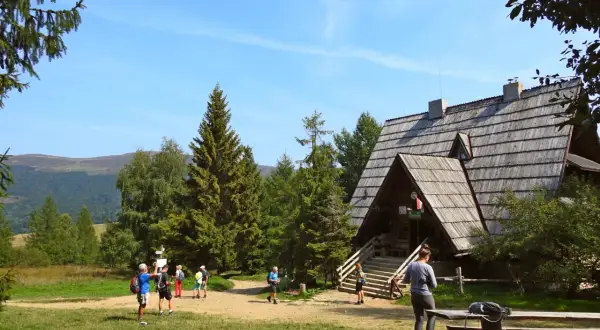 Bacówka PTTK pod Małą Rawką, drewniany schron turystyczny w otoczeniu zieleni, z kilkoma turystami na szlaku.