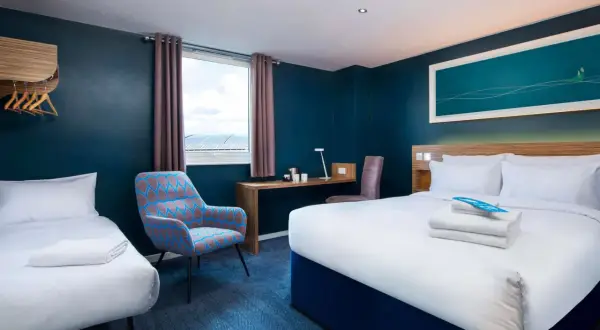 Pokój hotelowy z dwoma łóżkami, biurkiem i fotelem. Zastanawiasz się, ile kosztuje nocleg w Londynie?