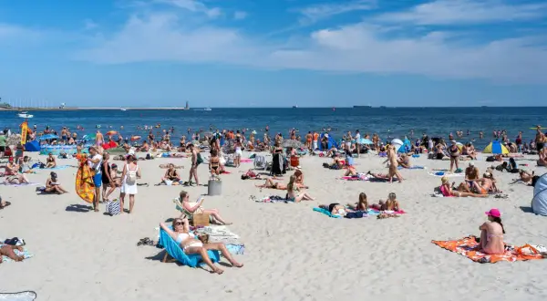 Tłum ludzi na plaży, opalanie, kąpiel w morzu. Zastanawiasz się, ile kosztuje nocleg nad morzem?