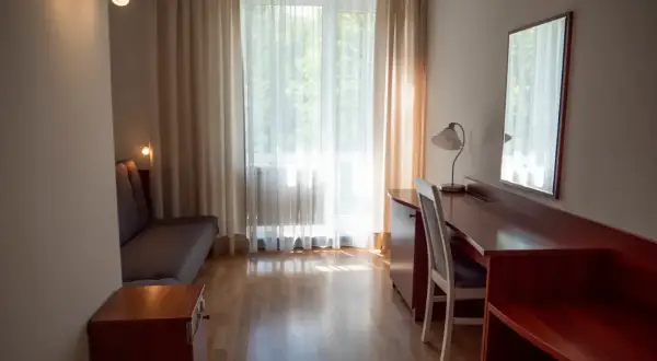 Pokój hotelowy z kanapą, biurkiem i lustrem. Zastanawiasz się, ile kosztuje nocleg w Zakopanem?
