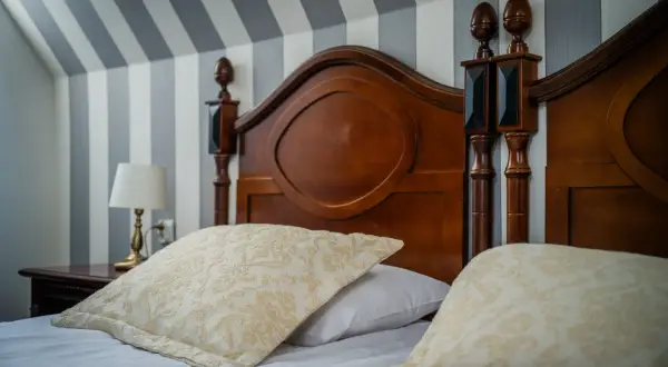 Przytulne łóżko z ozdobnymi poduszkami i drewnianym zagłówkiem. Idealne miejsce na nocleg, zastanawiasz się, ile wynosi ryczałt za nocleg?