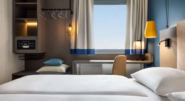 Nowoczesny pokój hotelowy z wygodnym łóżkiem, biurkiem i oknem. Zastanawiasz się, ile kosztuje nocleg w Krakowie?