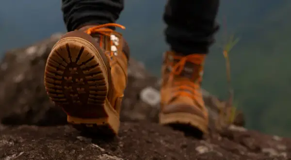 Brązowe buty trekkingowe z pomarańczowymi sznurówkami na kamienistym szlaku. Idealne buty w góry, zapewniające przyczepność i stabilność.