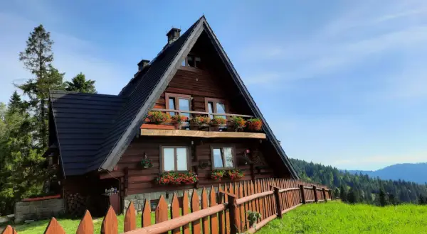 Drewniana bacówka na Maciejowej, otoczona zielenią i drewnianym płotem, z balkonem pełnym kwiatów.