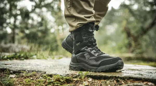 Czarne, wysokie buty trekkingowe na mokrej ścieżce. Idealne, jakie buty w góry jesienią, by stawiać pewne kroki w deszczu.
