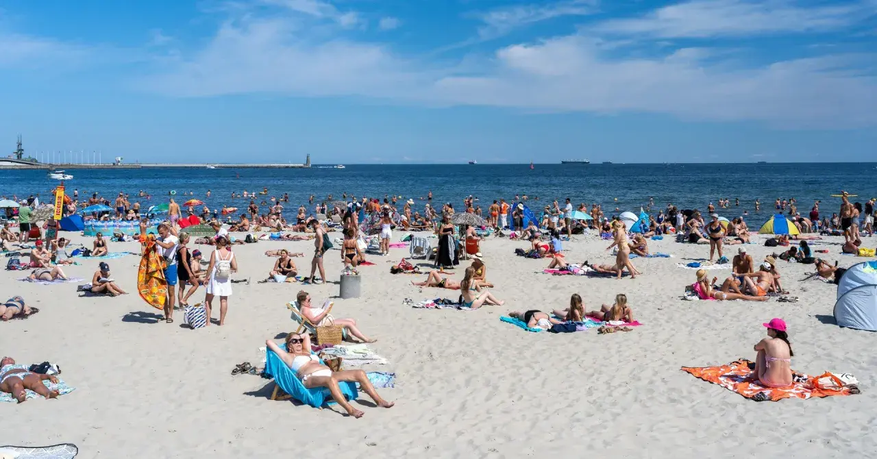 Tłum ludzi na plaży, opalanie, kąpiel w morzu. Zastanawiasz się, ile kosztuje nocleg nad morzem?