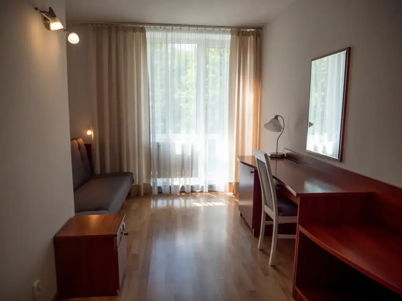 Pokój hotelowy z kanapą, biurkiem i lustrem. Zastanawiasz się, ile kosztuje nocleg w Zakopanem?