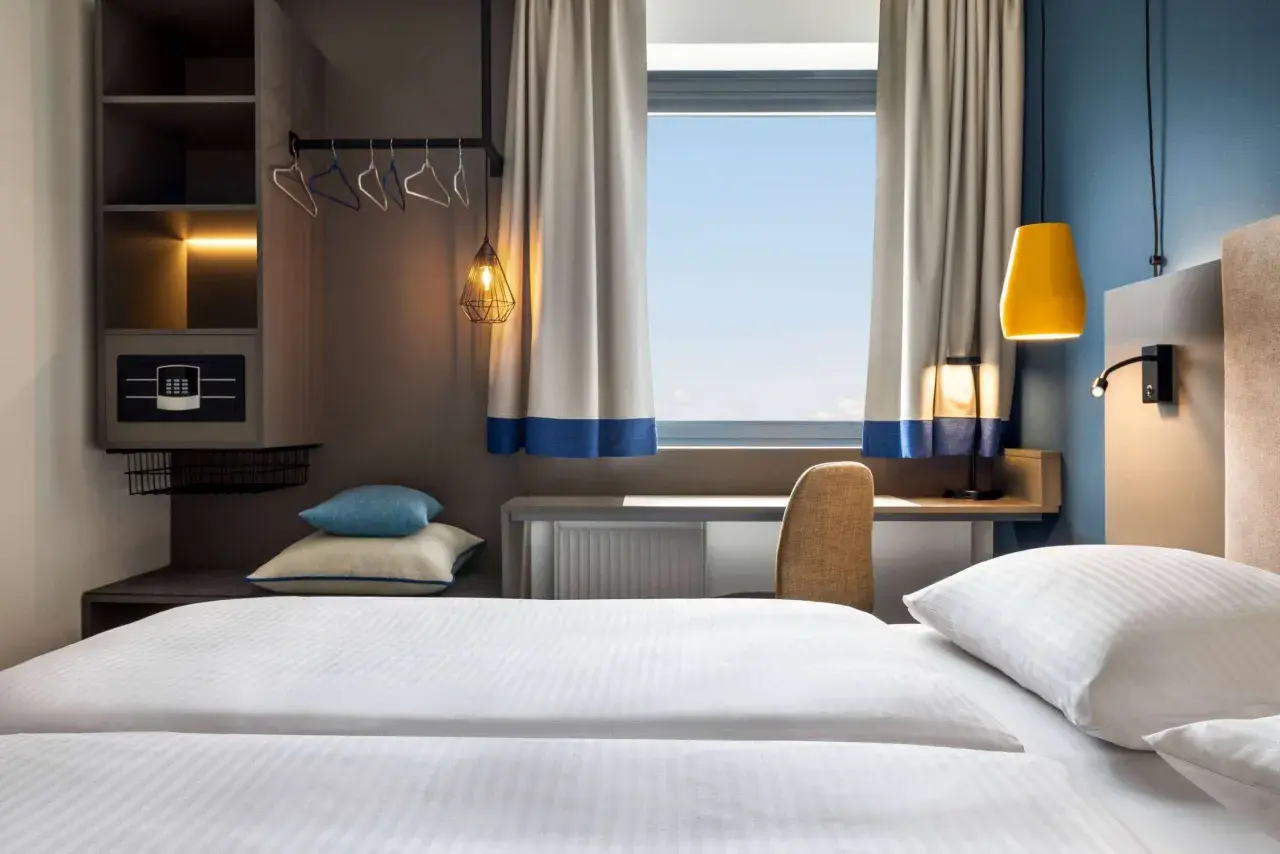Nowoczesny pokój hotelowy z wygodnym łóżkiem, biurkiem i oknem. Zastanawiasz się, ile kosztuje nocleg w Krakowie?