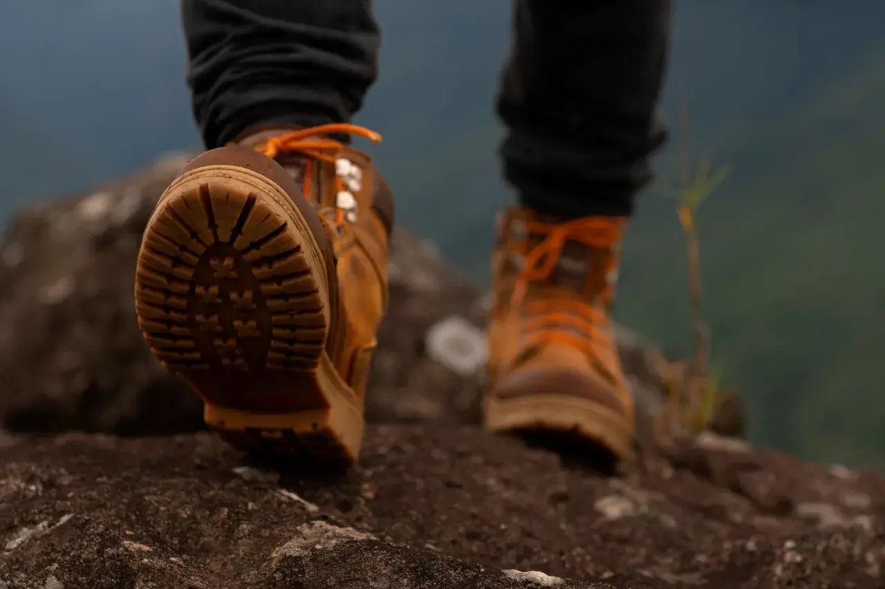 Brązowe buty trekkingowe z pomarańczowymi sznurówkami na kamienistym szlaku. Idealne buty w góry, zapewniające przyczepność i stabilność.