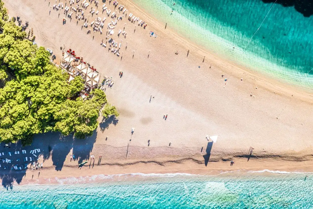 Piękna plaża w Chorwacji, idealne miejsce, gdzie szukać nocleg&oacute;w. Woda krystalicznie czysta, piasek złocisty, a drzewa dają cień.