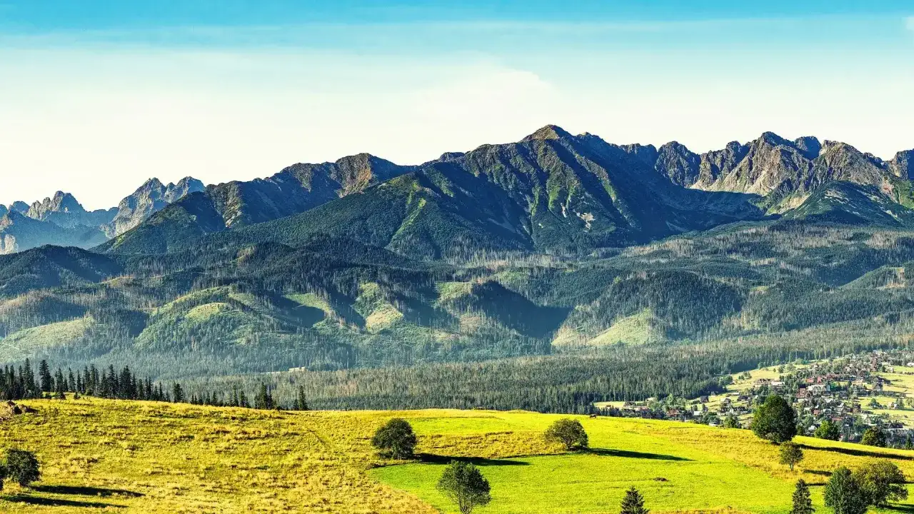 Widok na Tatry z zielonymi łąkami i lasami w tle, z widoczną wioską.