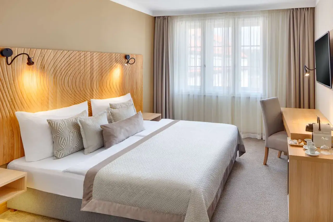 Przytulny pokój hotelowy z dużym łóżkiem i biurkiem. Zastanawiasz się, ile kosztuje nocleg w Pradze?