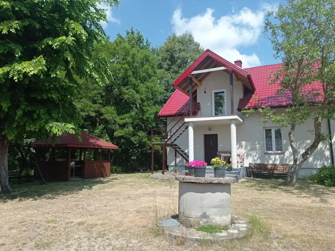 Dom z czerwoną dachem i altaną w ogrodzie. Idealne miejsce, gdzie szukać noclegu na wsi.