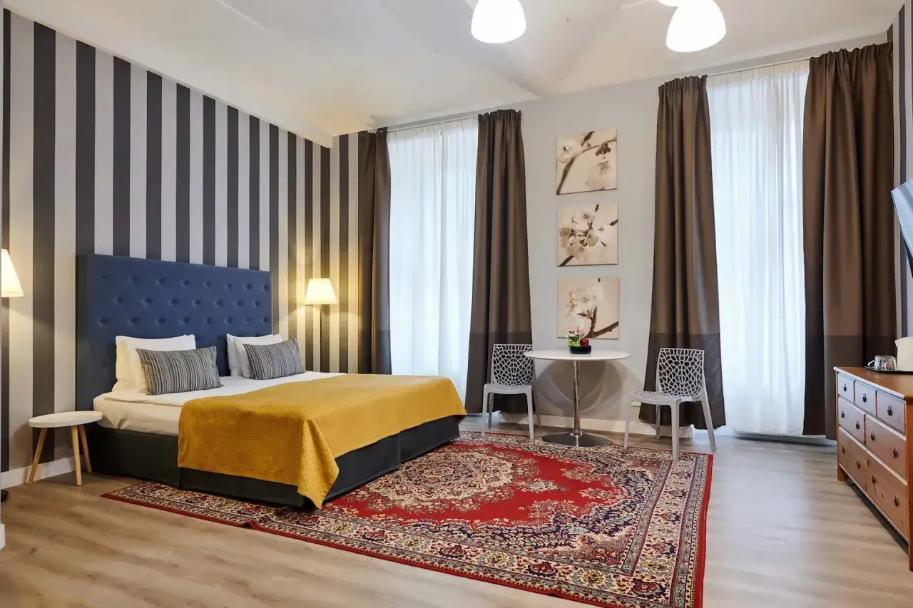 Przytulny pokój hotelowy z dużym łóżkiem, dywanem i stolikiem. Zastanawiasz się, ile kosztuje nocleg w Pradze?