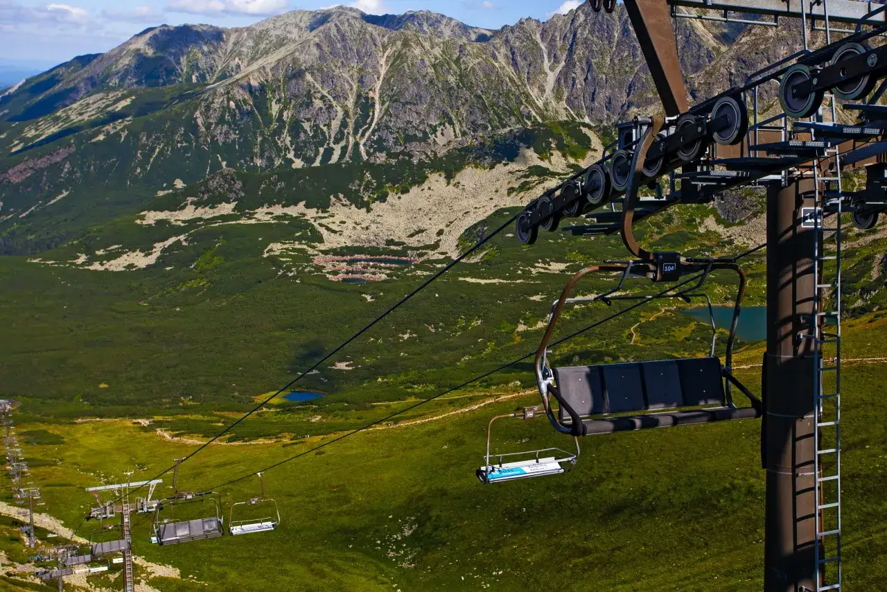 Kolejka linowa na Kasprowy Wierch w Tatrach. Krzesełka wspinają się pośród zielonych zboczy i skalistych szczytów.