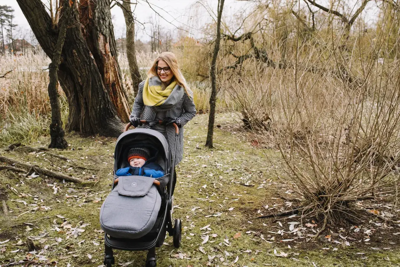 Mama z uśmiechem pcha wózek z 2-letnim dzieckiem. Idealny spacer, nawet jeśli nie gdzie w góry z dzieckiem 2 letnim.