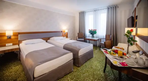 Pokój hotelowy z dwoma łóżkami, stolikiem z owocami i różami. Zastanawiasz się, ile kosztuje nocleg w hotelu?