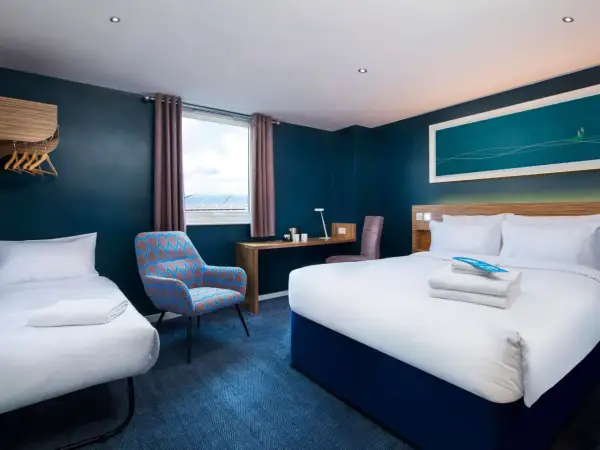 Pokój hotelowy z dwoma łóżkami, biurkiem i fotelem. Zastanawiasz się, ile kosztuje nocleg w Londynie?