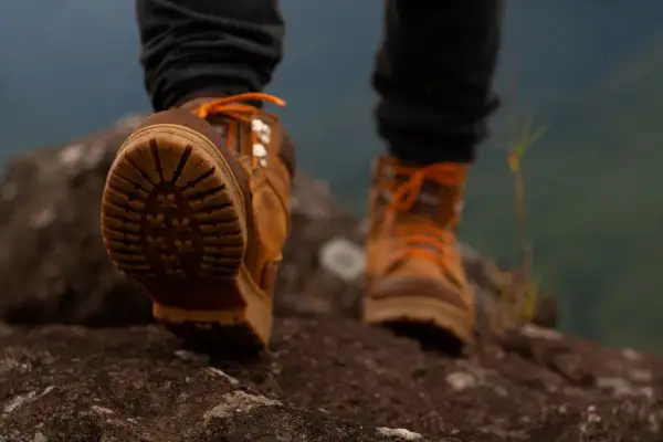 Brązowe buty trekkingowe z pomarańczowymi sznurówkami na kamienistym szlaku. Idealne buty w góry, zapewniające przyczepność i stabilność.
