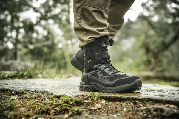 Czarne, wysokie buty trekkingowe na mokrej ścieżce. Idealne, jakie buty w góry jesienią, by stawiać pewne kroki w deszczu.